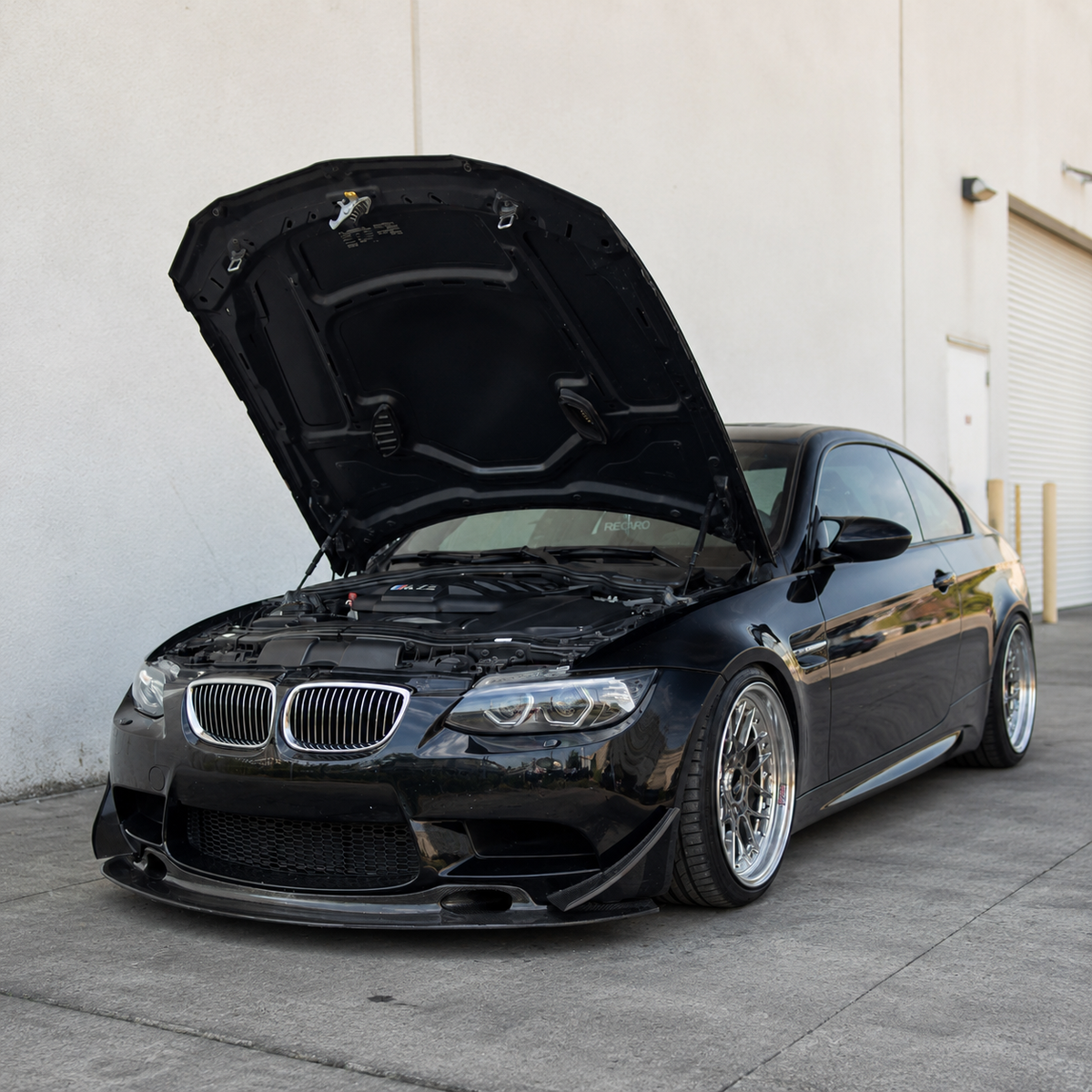 AlpineX Dynamics GT4 Style Carbon Fiber Canard installed on a black BMW E9X M3, shown from the front three-quarter view with the hood open.