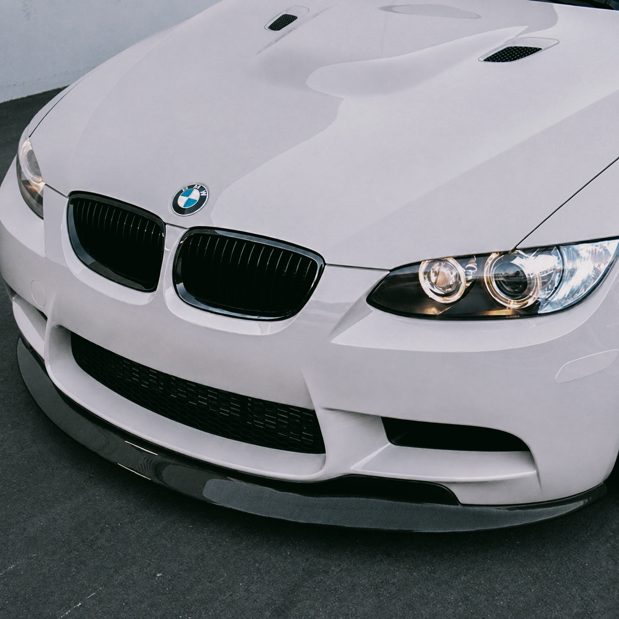 AlpineX Dynamics GTS Style Carbon Fiber Front Lip installed on a BMW E9X M3, shown in a close-up view highlighting its glossy carbon fiber finish and detailed fitment.