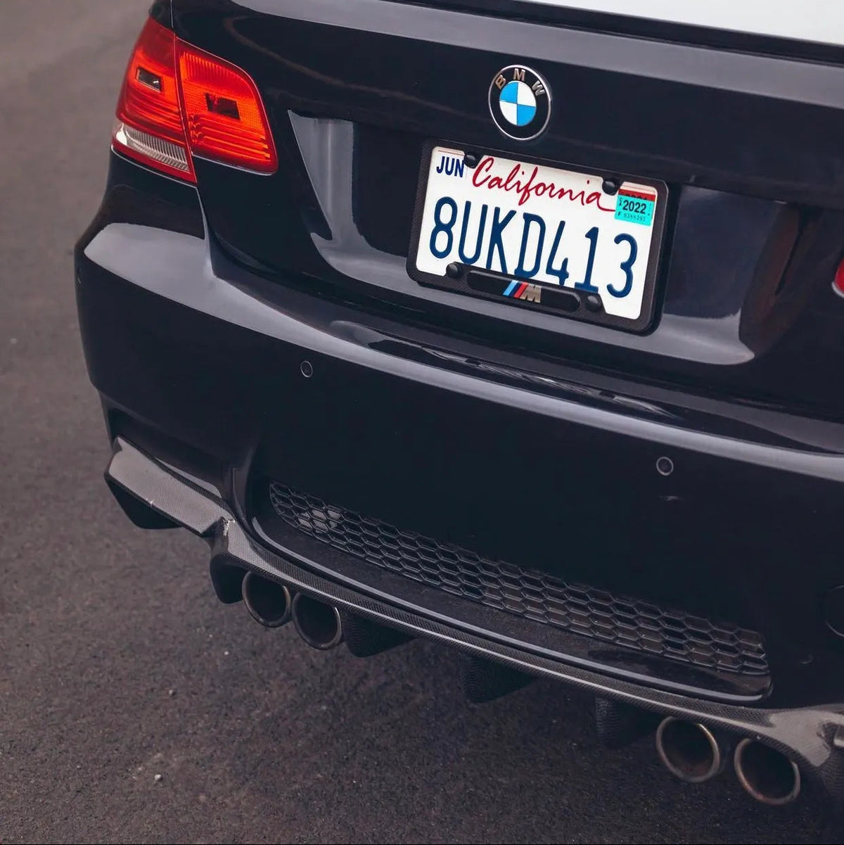 Close-up rear view of the AlpineX Dynamics GTS style carbon fiber rear diffuser for BMW E92/E93 M3, showing the diffuser fins and quad exhaust outlets beneath a black rear bumper