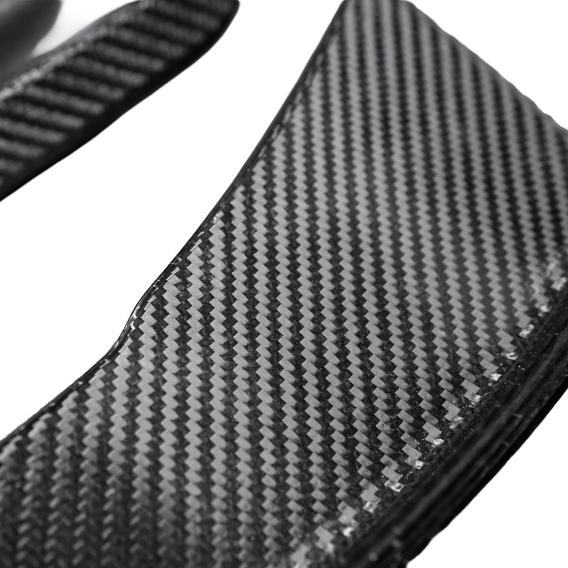 Close-up of the woven carbon fiber surface and curved edge of an AlpineX Dynamics GT4 style canard for BMW E9X M3 on a white background