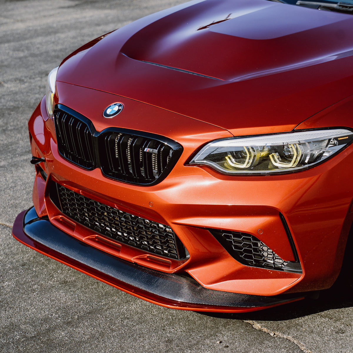 Front view of an orange BMW F87 M2 Competition with adjustable carbon fiber front splitter
