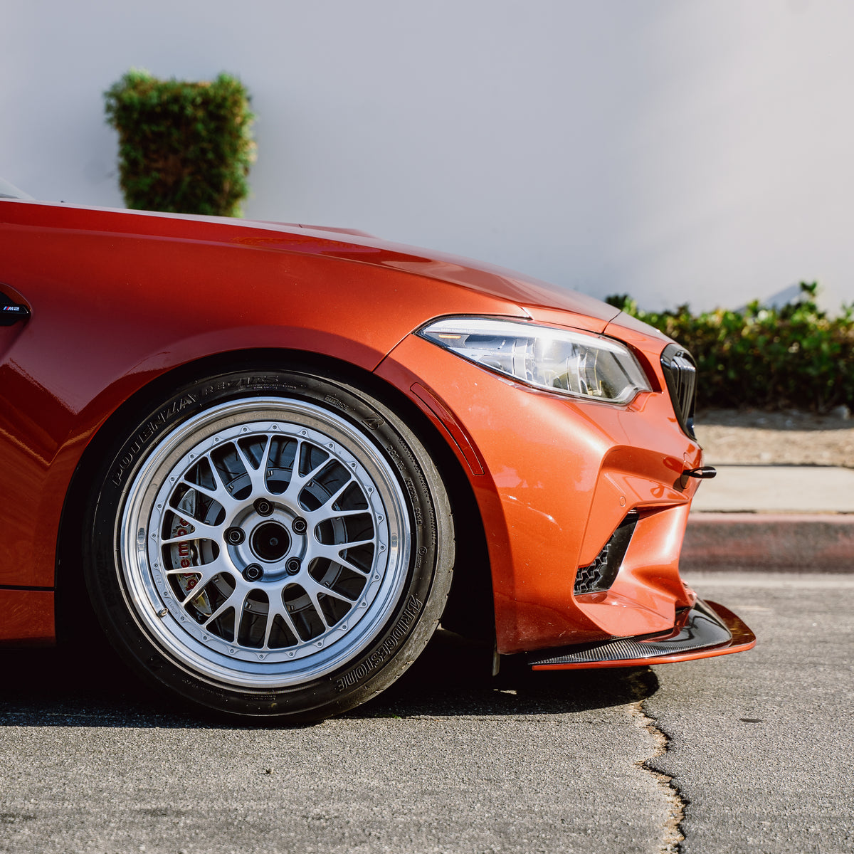 Side view of an orange BMW F87 M2 Competition showing the front splitter extension