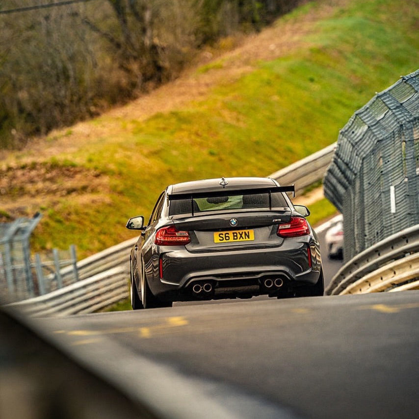 BMW F87 M2 with Ring Spec Wing V2 viewed from the rear on track