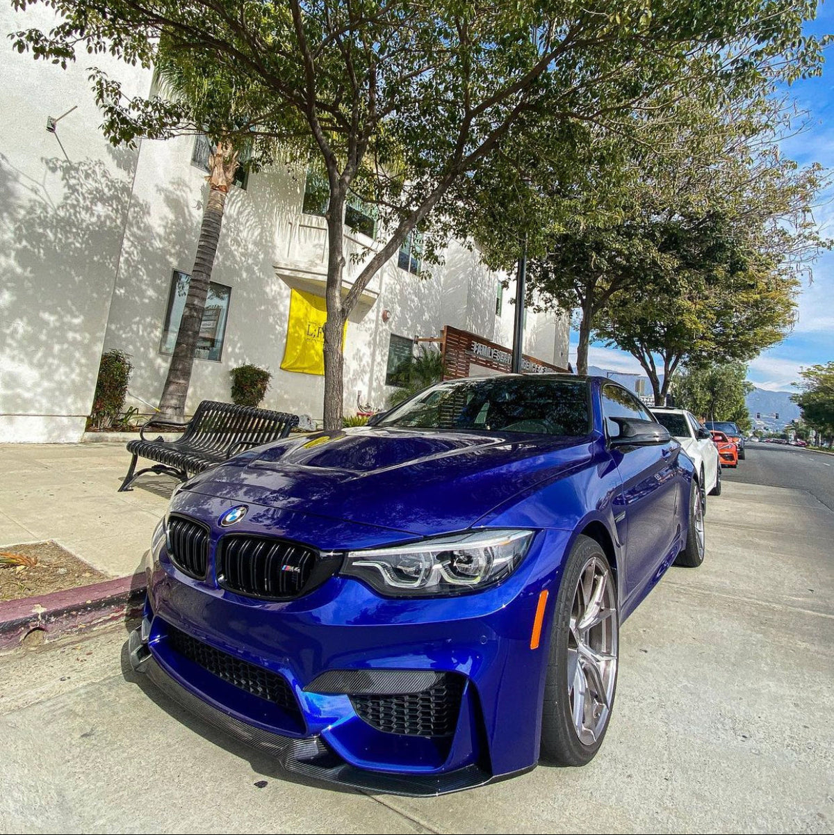 Front three-quarter street view of a blue BMW fitted with the AlpineX Dynamics CS style carbon fiber front lip for the F8X M3 and M4