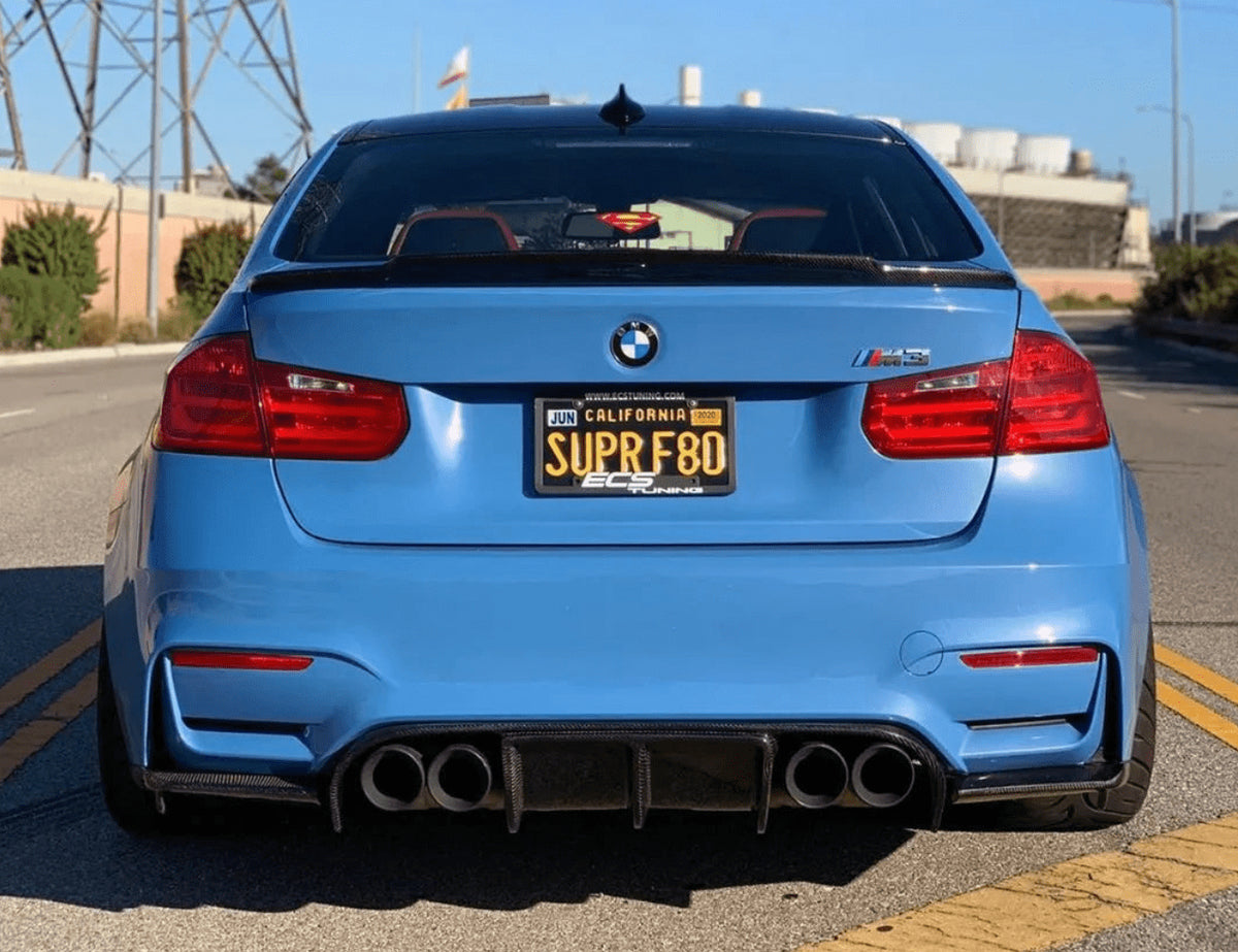 Rear view of a blue BMW F80 M3 with the AlpineX Dynamics V style three-piece carbon fiber rear diffuser for F8X M3/M4, showing central fins and side extensions around quad exhaust outlets