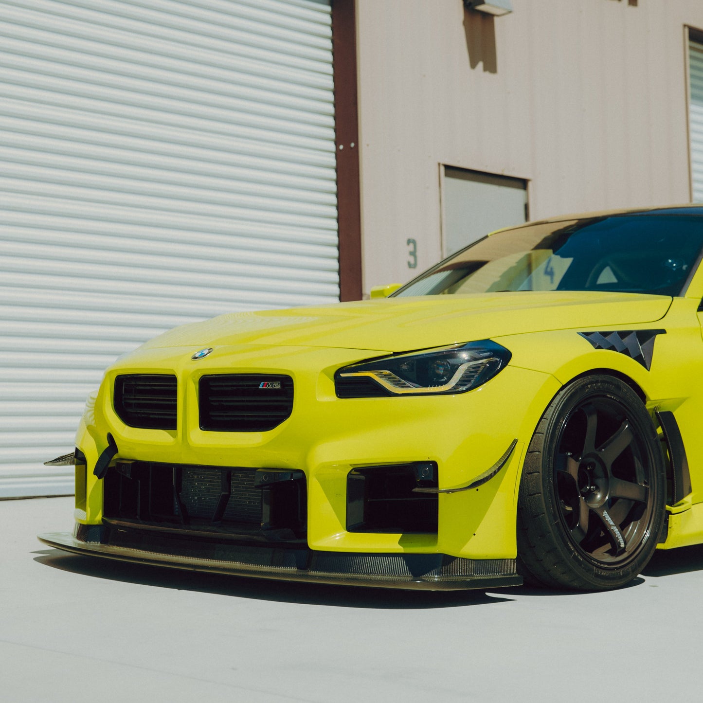 Low front three-quarter view of a yellow BMW G87 M2 with carbon fiber canards and GT4+ front aero