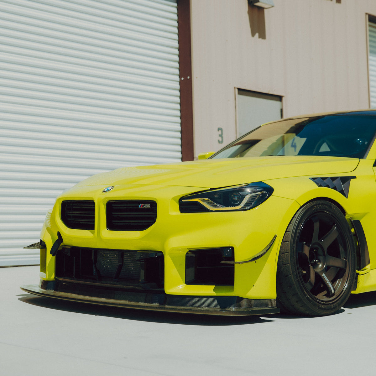 Low front three-quarter view of a yellow BMW G87 M2 with carbon fiber canards and GT4+ front aero