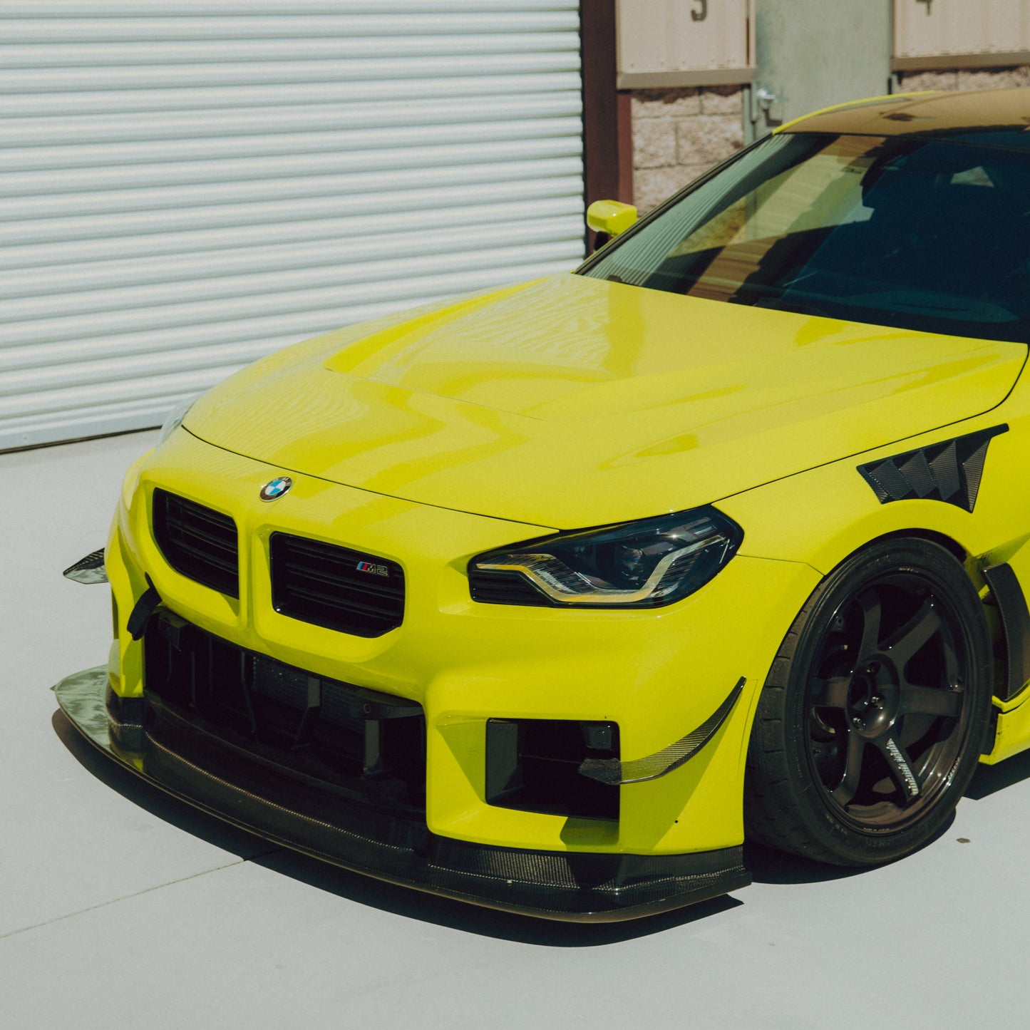 Front three-quarter view of a yellow BMW G87 M2 equipped with GT4+ carbon fiber canards