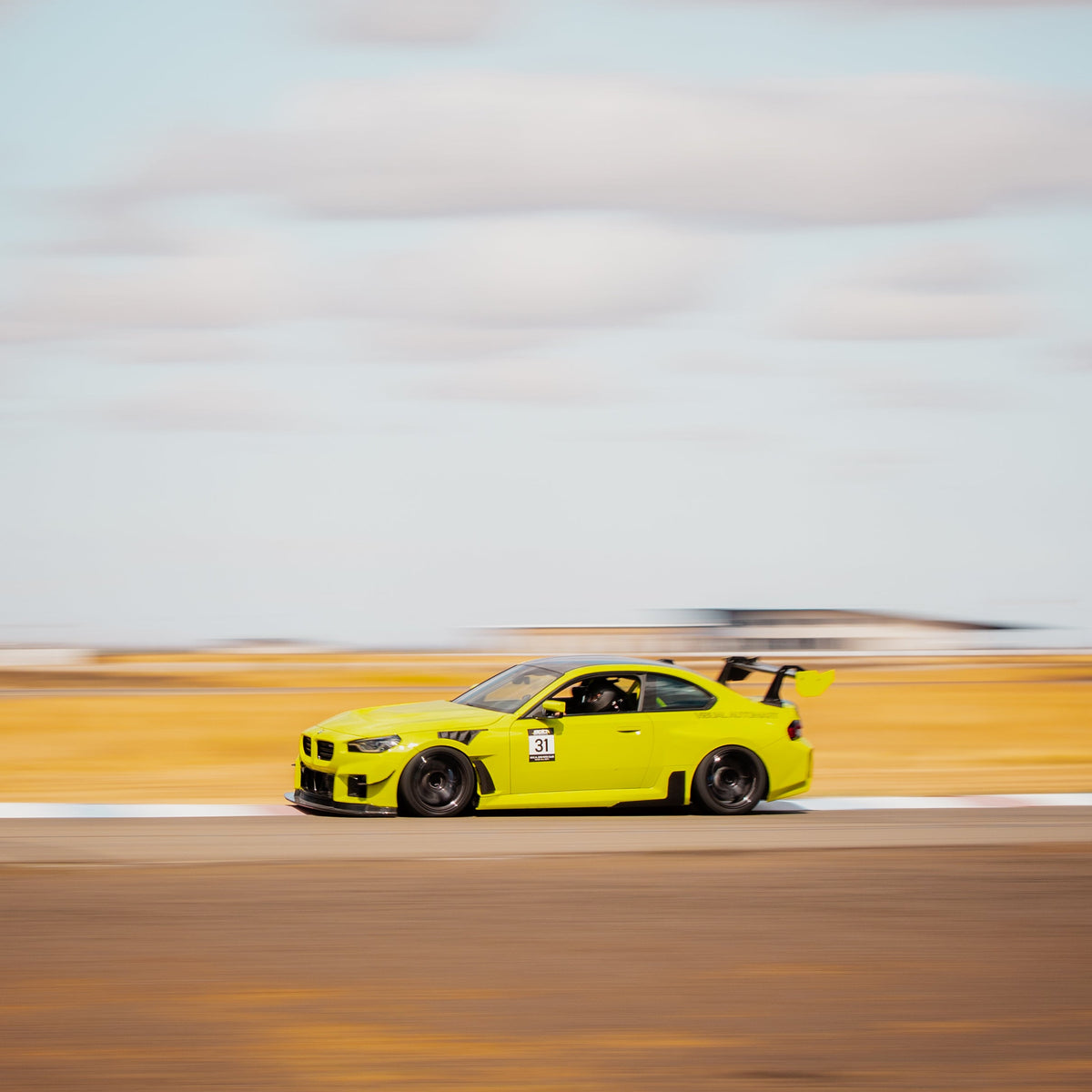 Side profile of a Sao Paulo Yellow BMW G87 M2 with the carbon fiber swan-neck rear wing on track