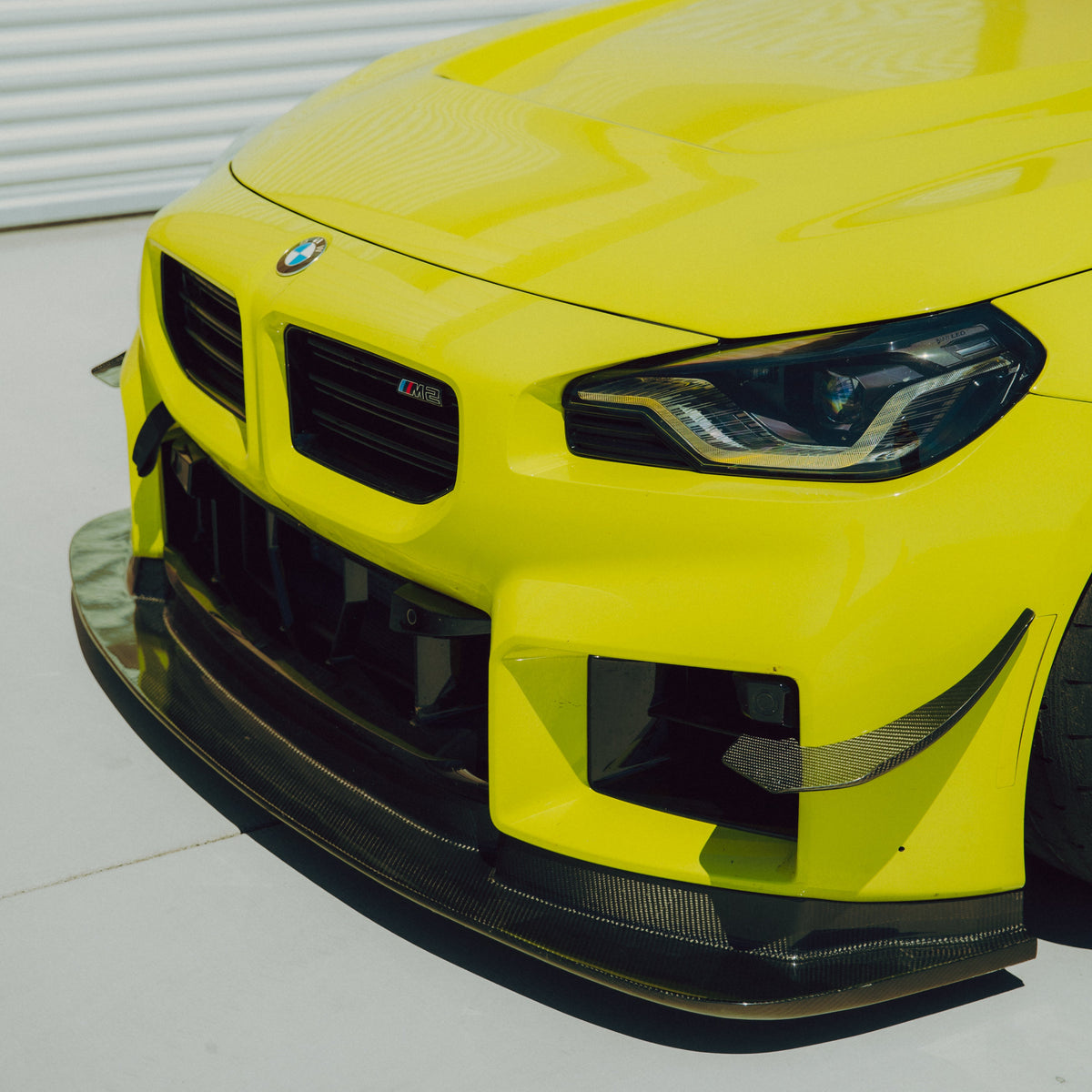 Upper front three-quarter view of a BMW G87 M2 with GT4+ carbon fiber canards and front splitter
