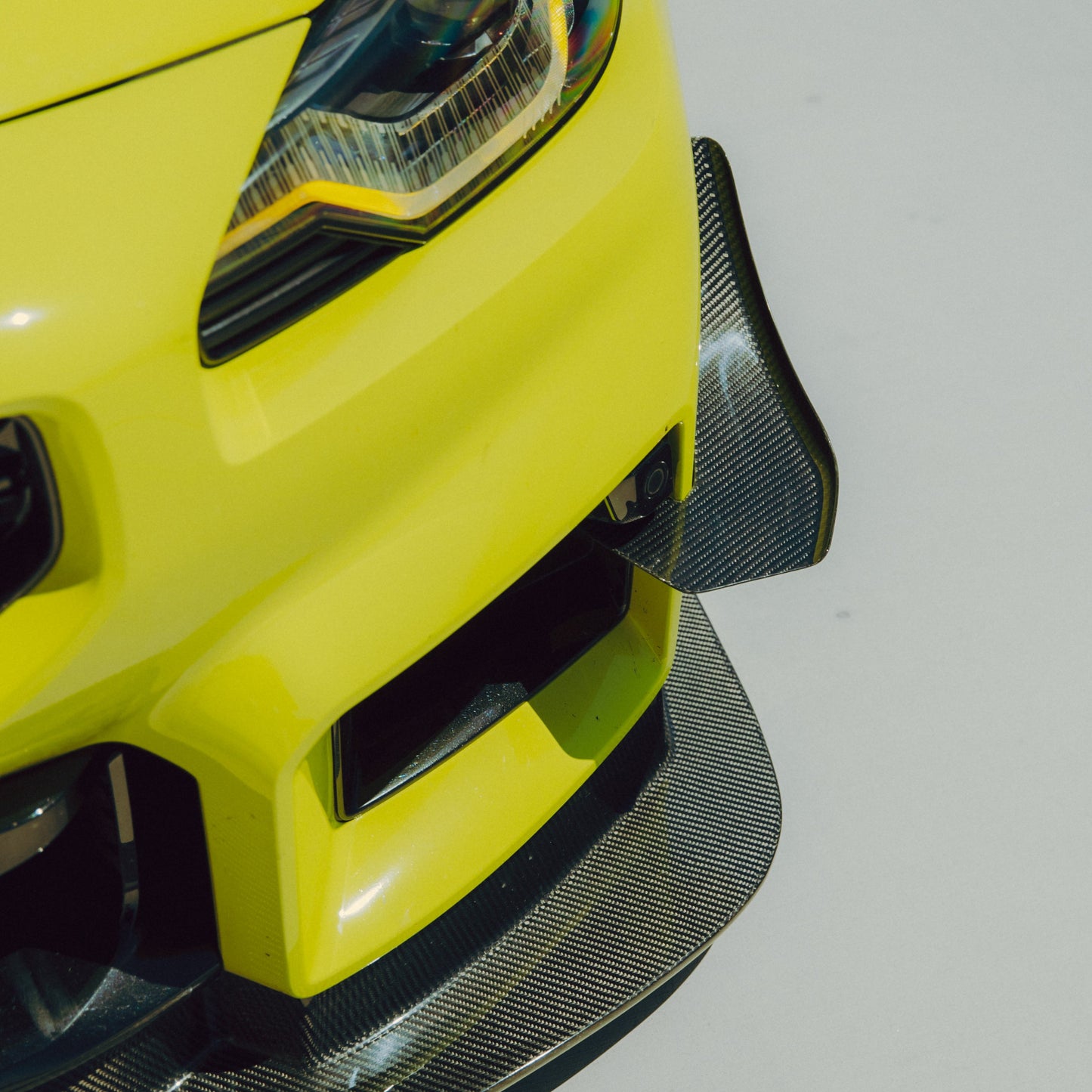 Close-up of a BMW G87 M2 GT4+ carbon fiber canard positioned above the front splitter