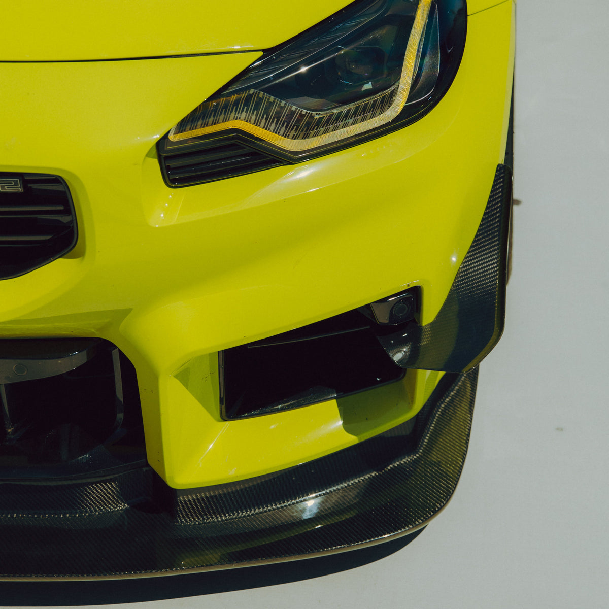 Installed detail of the carbon fiber canard following the outer corner of the BMW G87 M2 front bumper