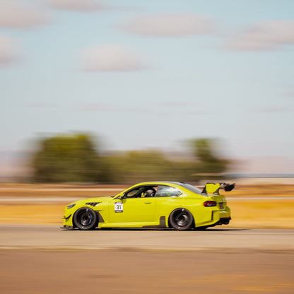 Rear three-quarter motion view of a BMW G87 M2 showing the GT4+ rear wing during track driving