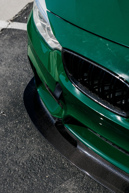 Close-up of the GT4 V2 carbon fiber front splitter installed on a green BMW F82 M4