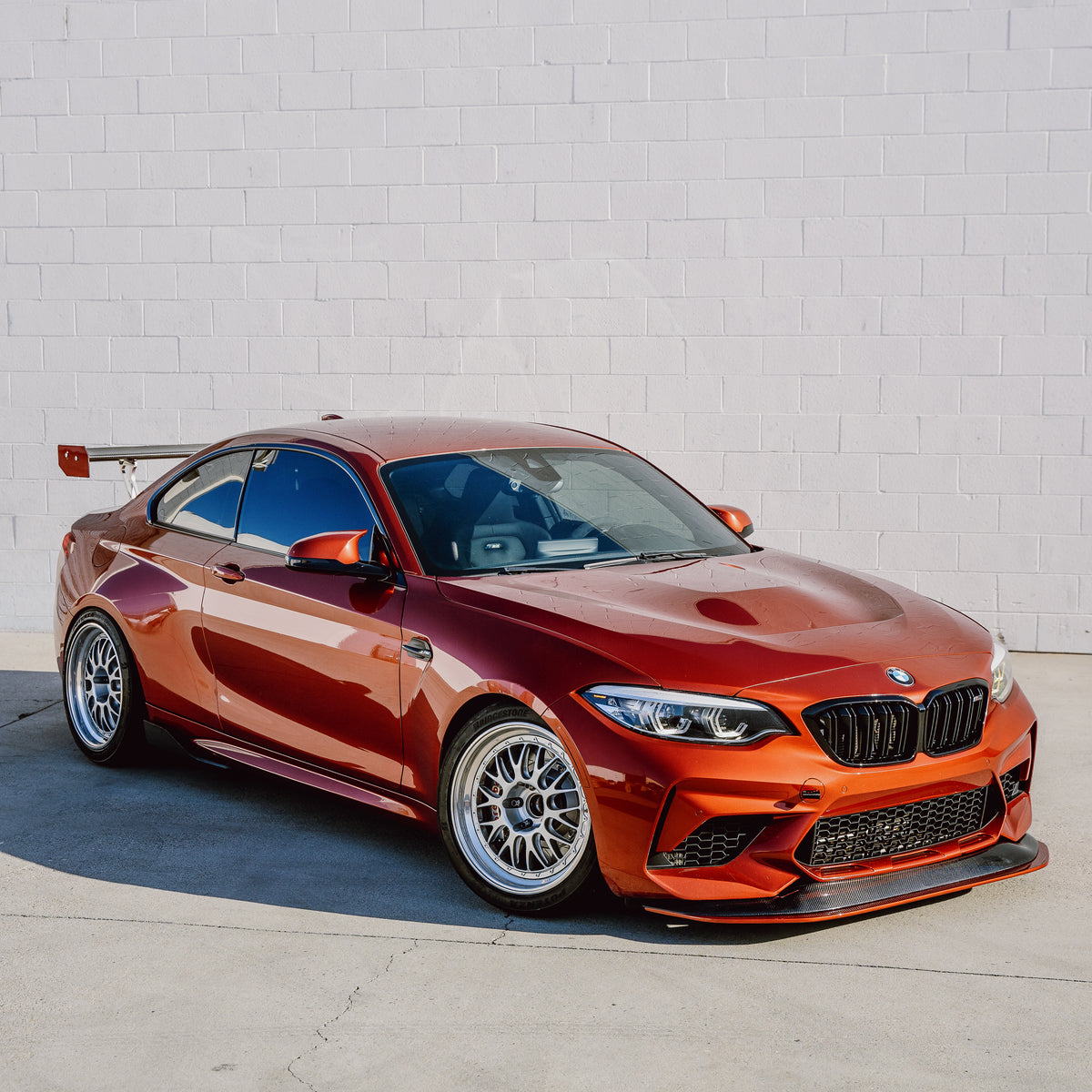 Orange BMW F87 M2 Competition with adjustable front splitter in a full three-quarter view