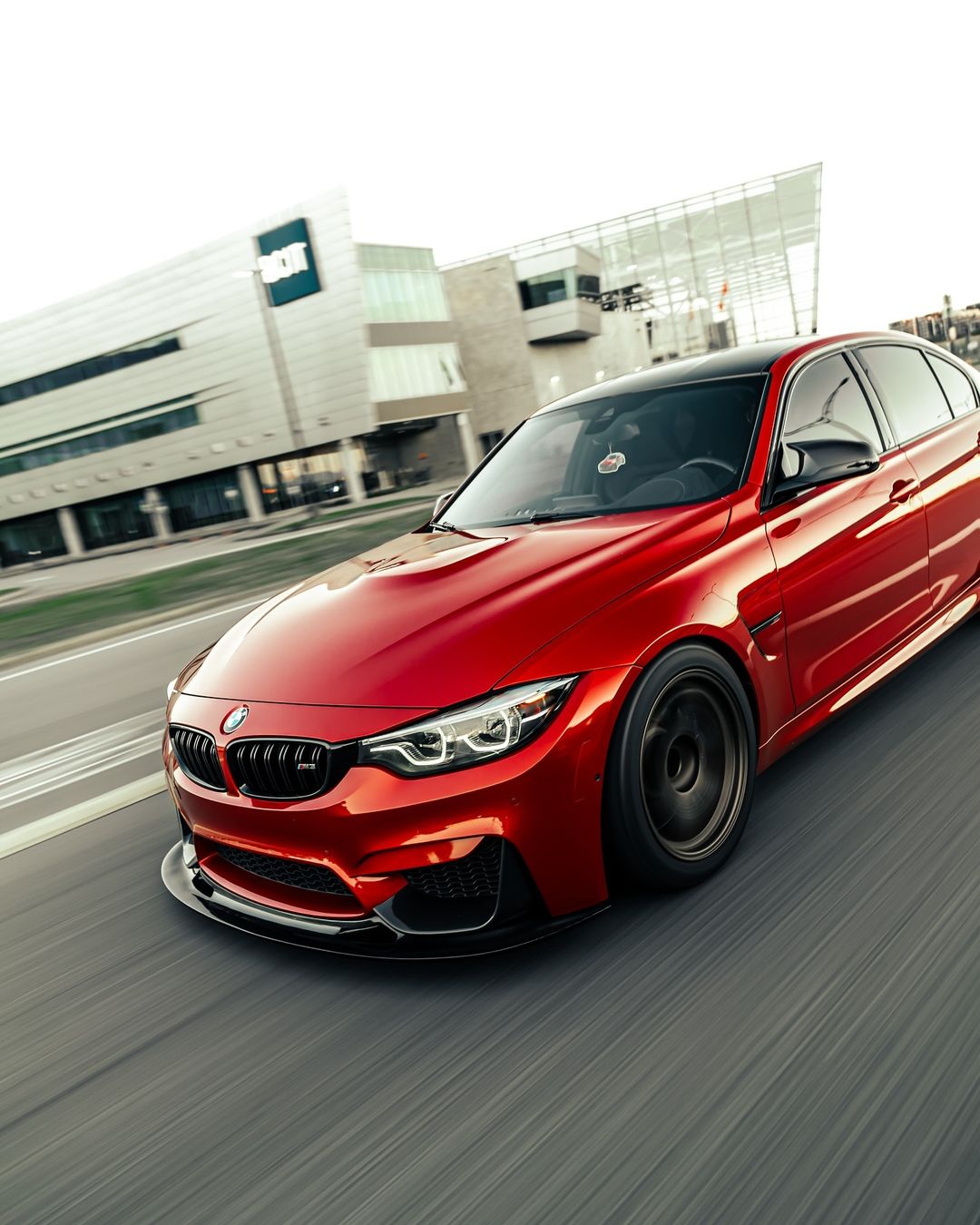 Red BMW F80 M3 with GT4 V1 carbon fiber front splitter in a front three-quarter rolling view