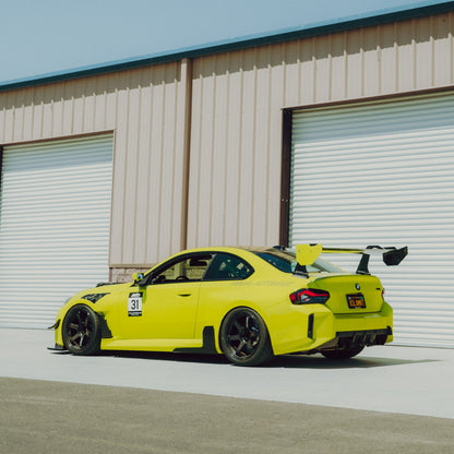 Rear three-quarter view of a Sao Paulo Yellow BMW G87 M2 with the GT4+ swan-neck rear wing