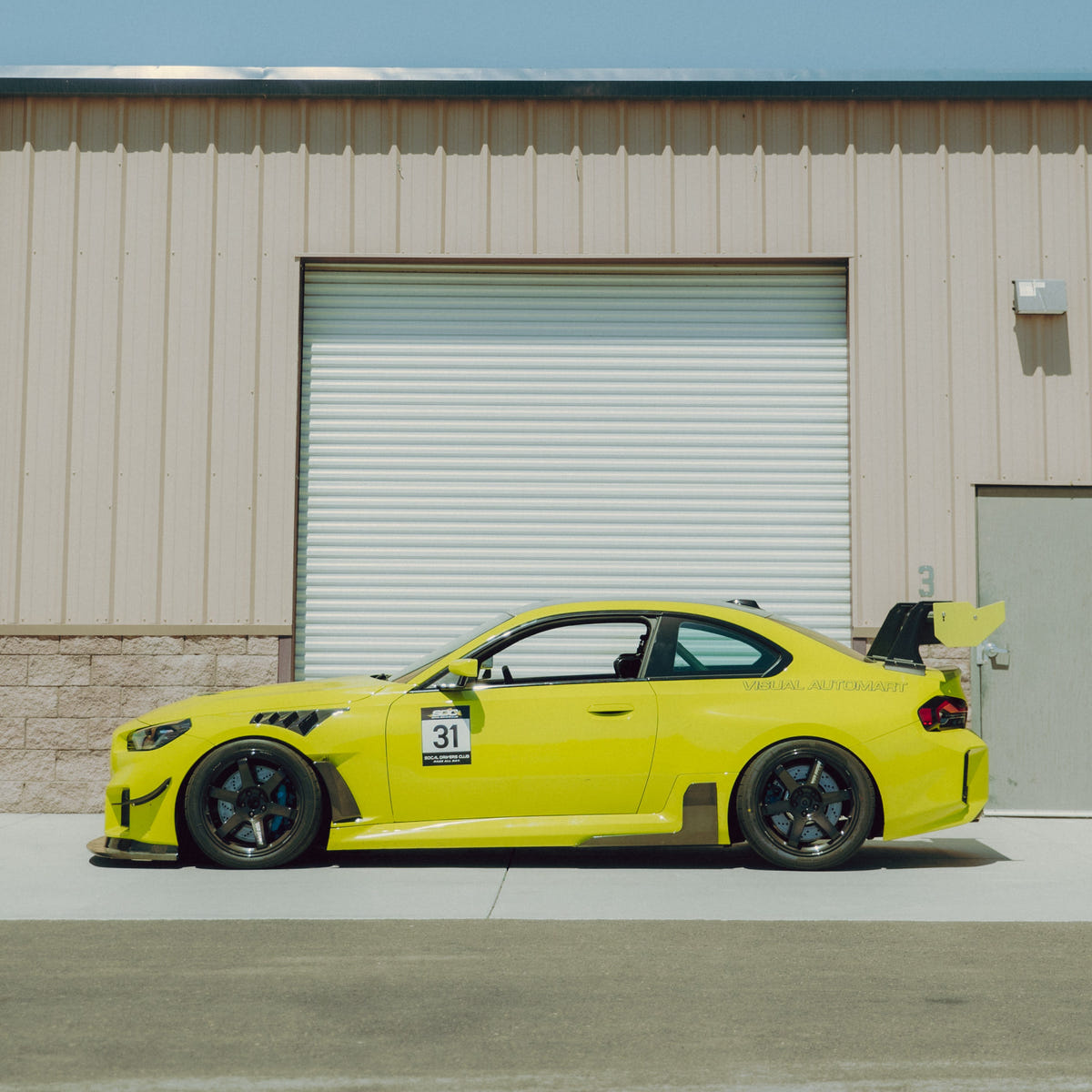 Full side profile of a Sao Paulo Yellow BMW G87 M2 with the GT4+ carbon fiber rear wing