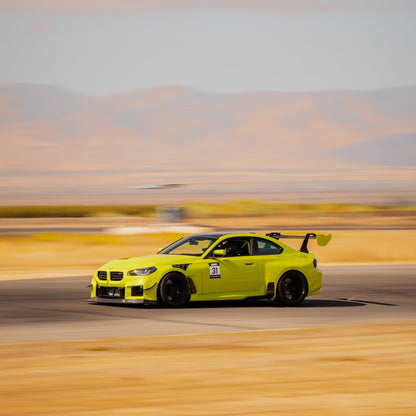 Sao Paulo Yellow BMW G87 M2 driving on track with the GT4+ carbon fiber swan-neck rear wing