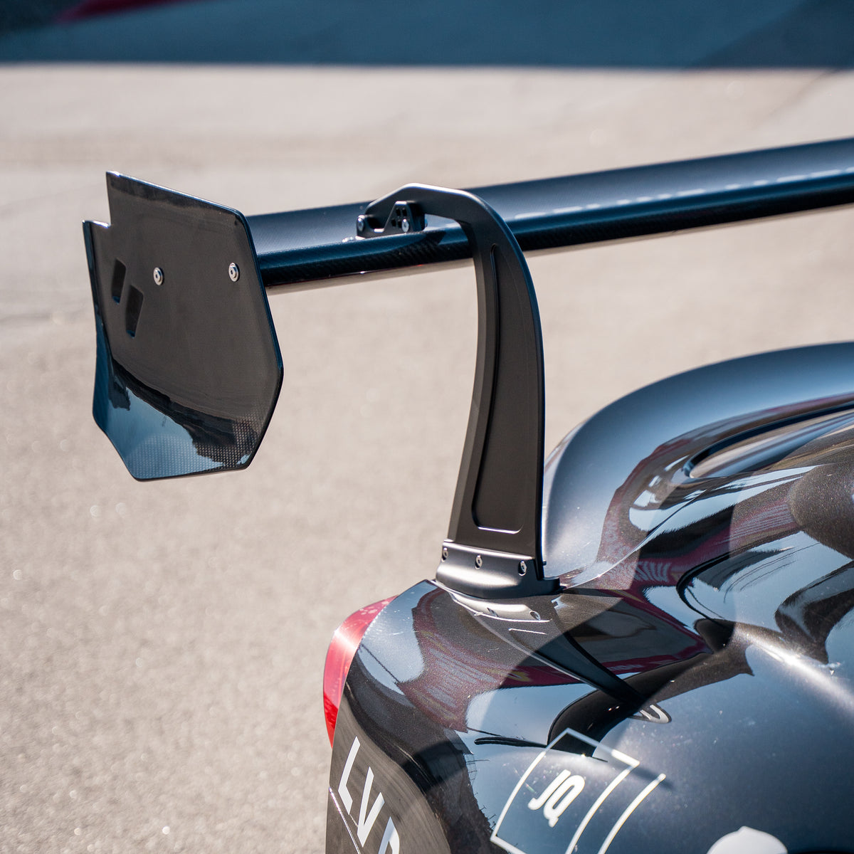 Close-up of the RM Engineering GT4+ rear wing on a Toyota GR Supra A90/A91, showing the carbon fiber endplate, curved upright and bolted trunk mounting base