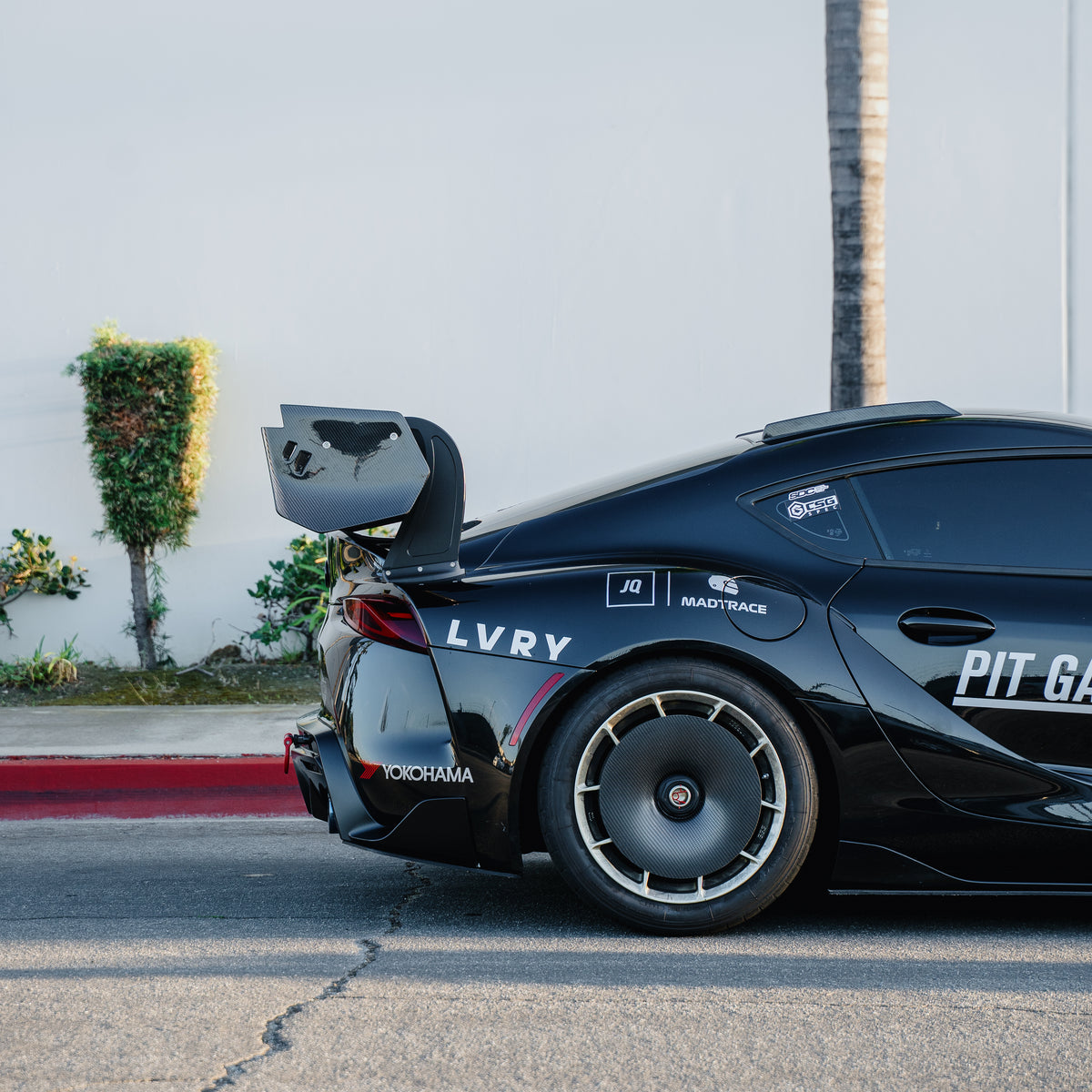 Side view of the rear quarter of a black Toyota GR Supra A90/A91, showing the RM Engineering GT4+ carbon fiber rear wing, endplate and rear wheel