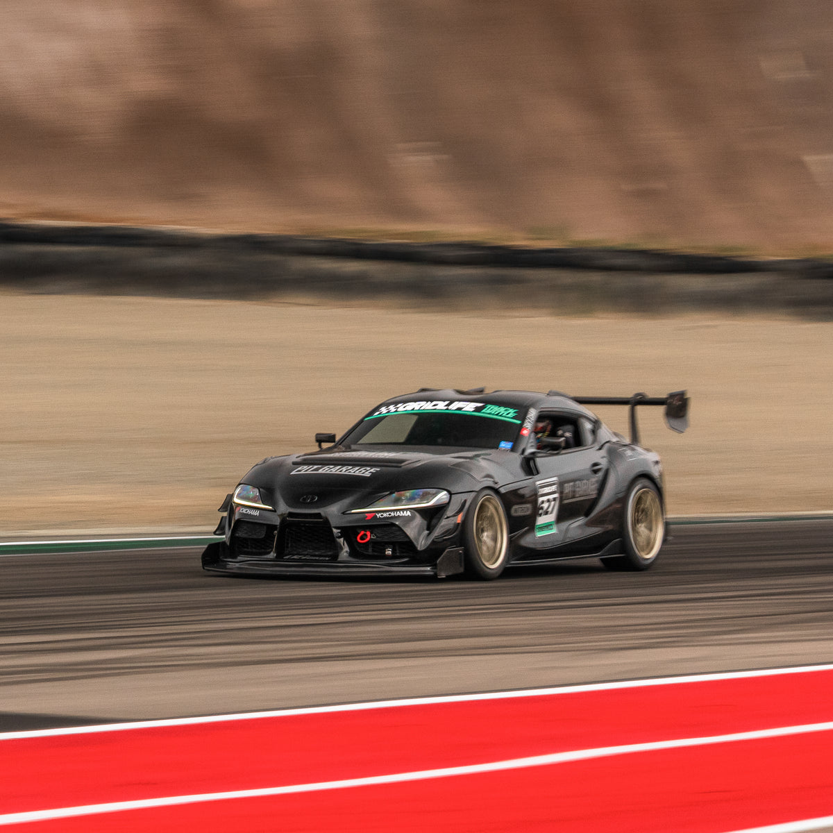 Black Toyota GR Supra race car with the RM Engineering GT4+ front splitter and rear wing in a front three-quarter track action view