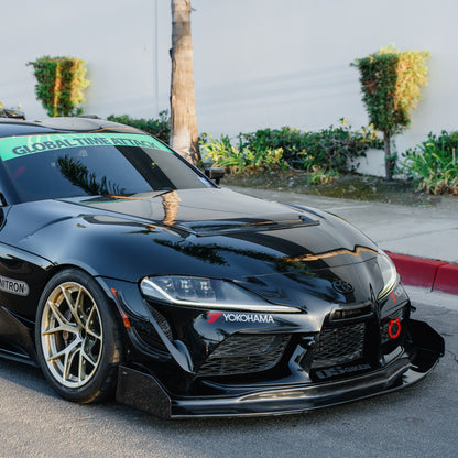 RM Engineering GT4+ front splitter kit on a black Toyota GR Supra A90, showing the carbon fiber splitter and tall endplates from a front three-quarter angle
