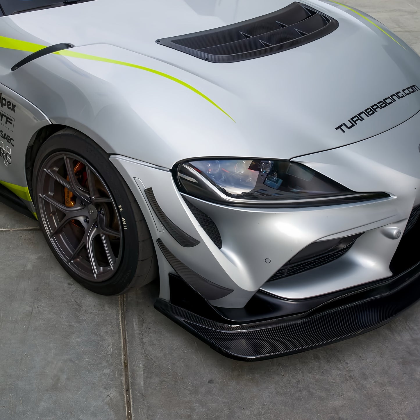 Front-end detail of a Toyota GR Supra A90 with GT4+ front lip, tunneled splitter, canards and carbon fiber hood vent