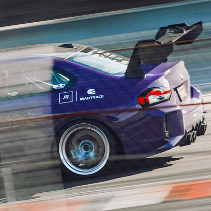 Ultraviolet BMW G87 M2 running on track with the GT4+ swan-neck rear wing viewed from the rear